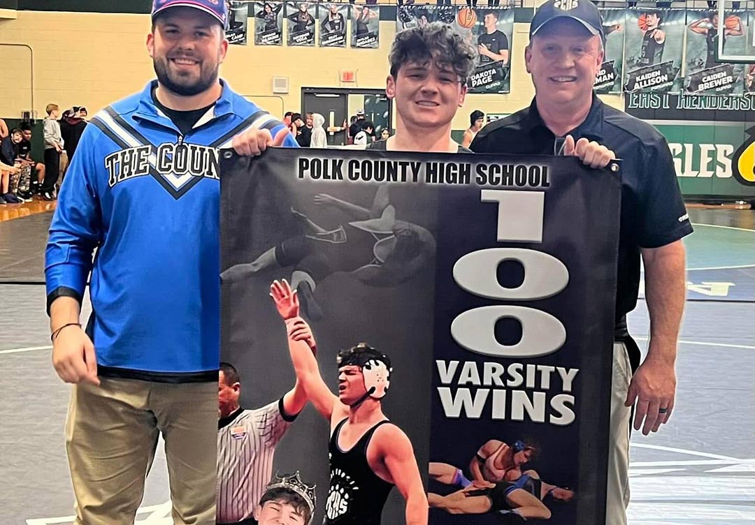 Polk County head wrestling coach Thomas Hensley, left, and assistant coach Mark Emory, right. celebrate Jacob Ed's 100th career wn (photo courtesy Polk County Wrestling)