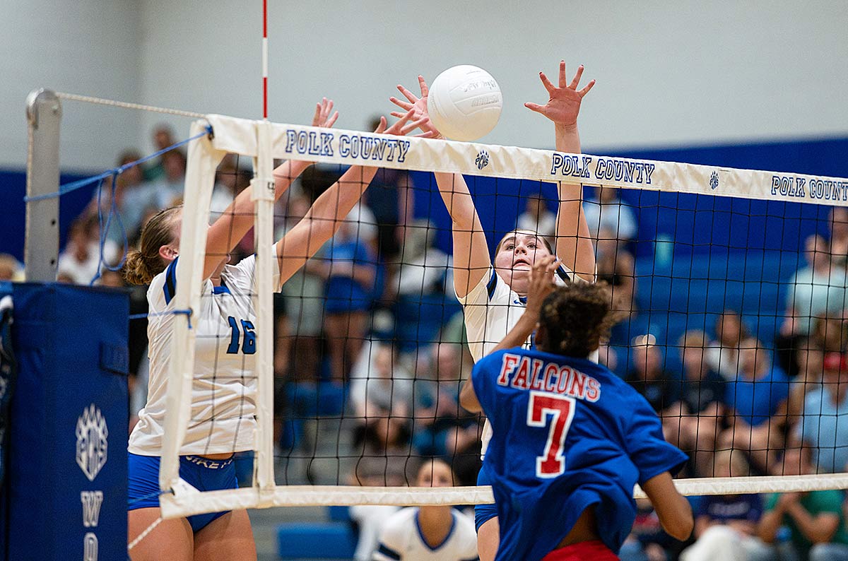 Polk County's Kenzie Alm, left, and Emily Nance throw up a block of West Henderson's Giselle White during Tuesday's match